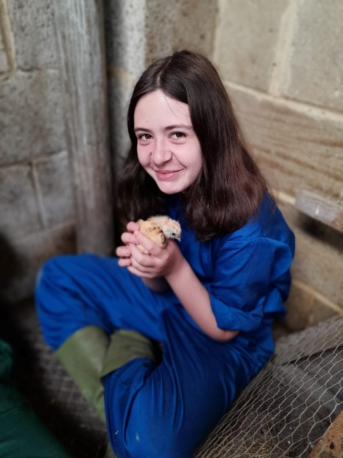 Girl in blue overalls holding a chicken and smiling