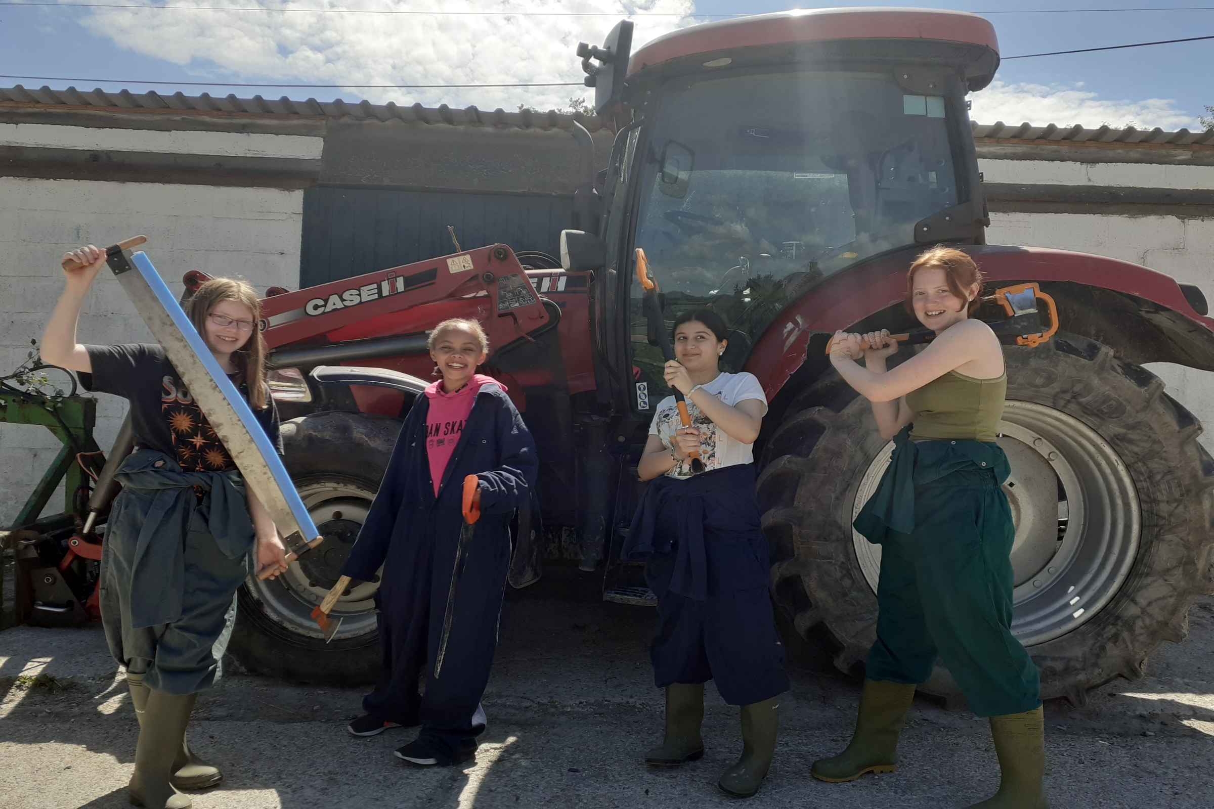 Four girls posing in front of a tractor with farming tools