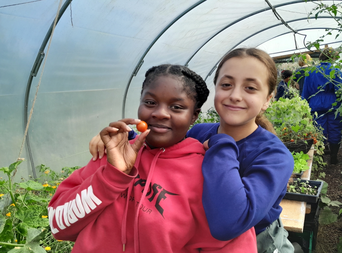 girls smiling in polytunnel with a tomato