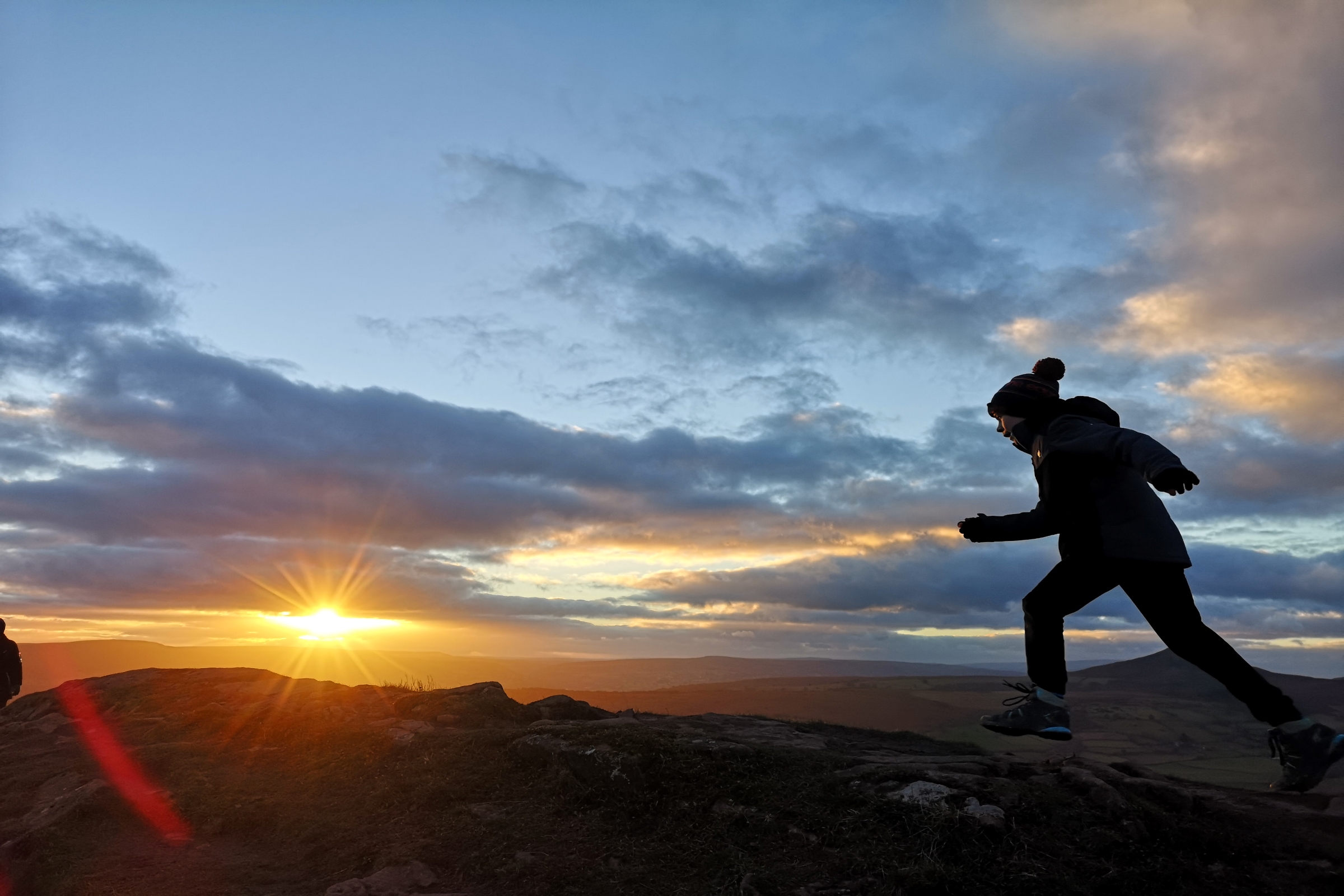 Silhouette of young person running on hilltop at sunset