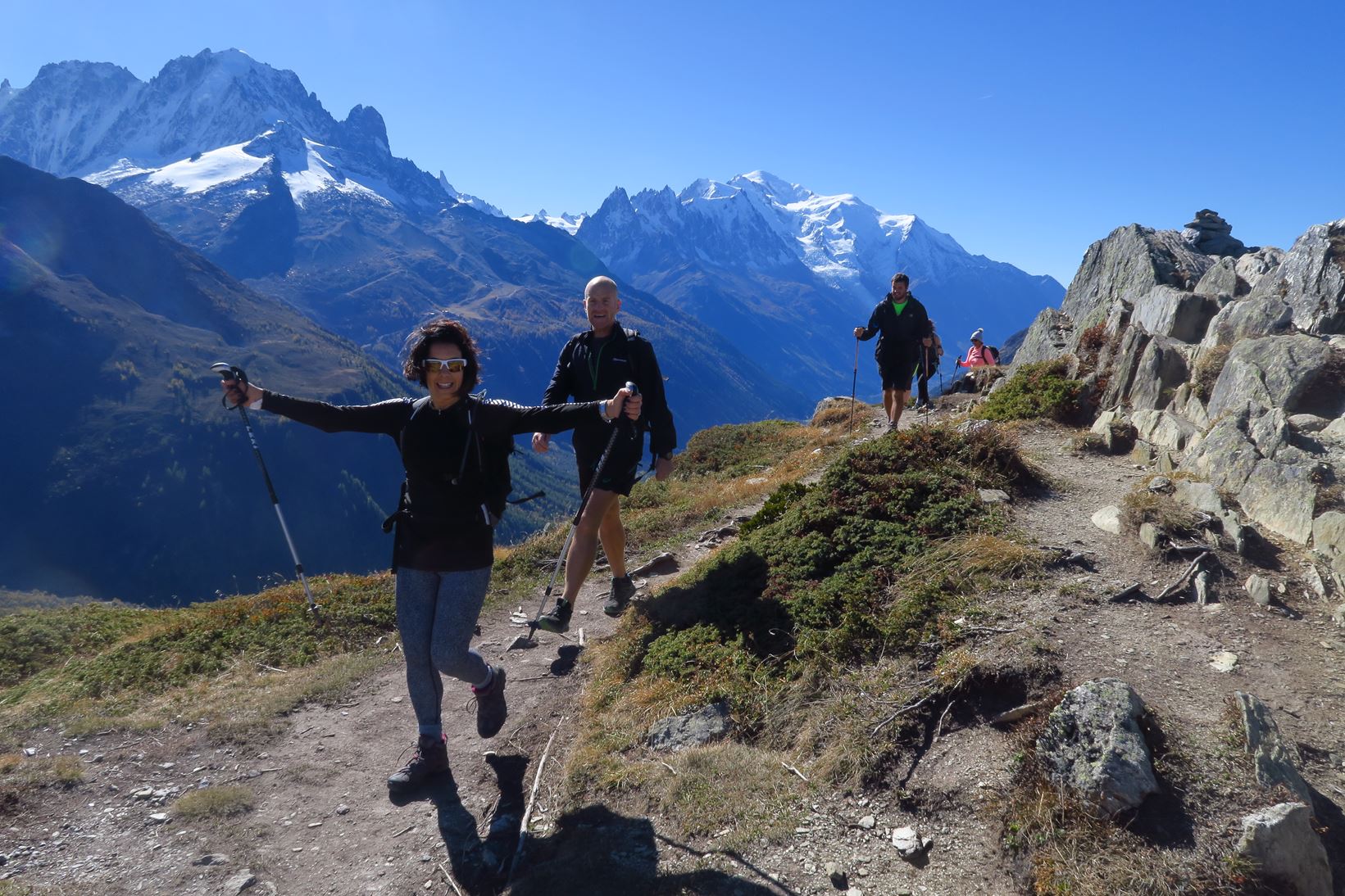 Walkers smiling at the camera, surrounded by the Alpes and blue skies.