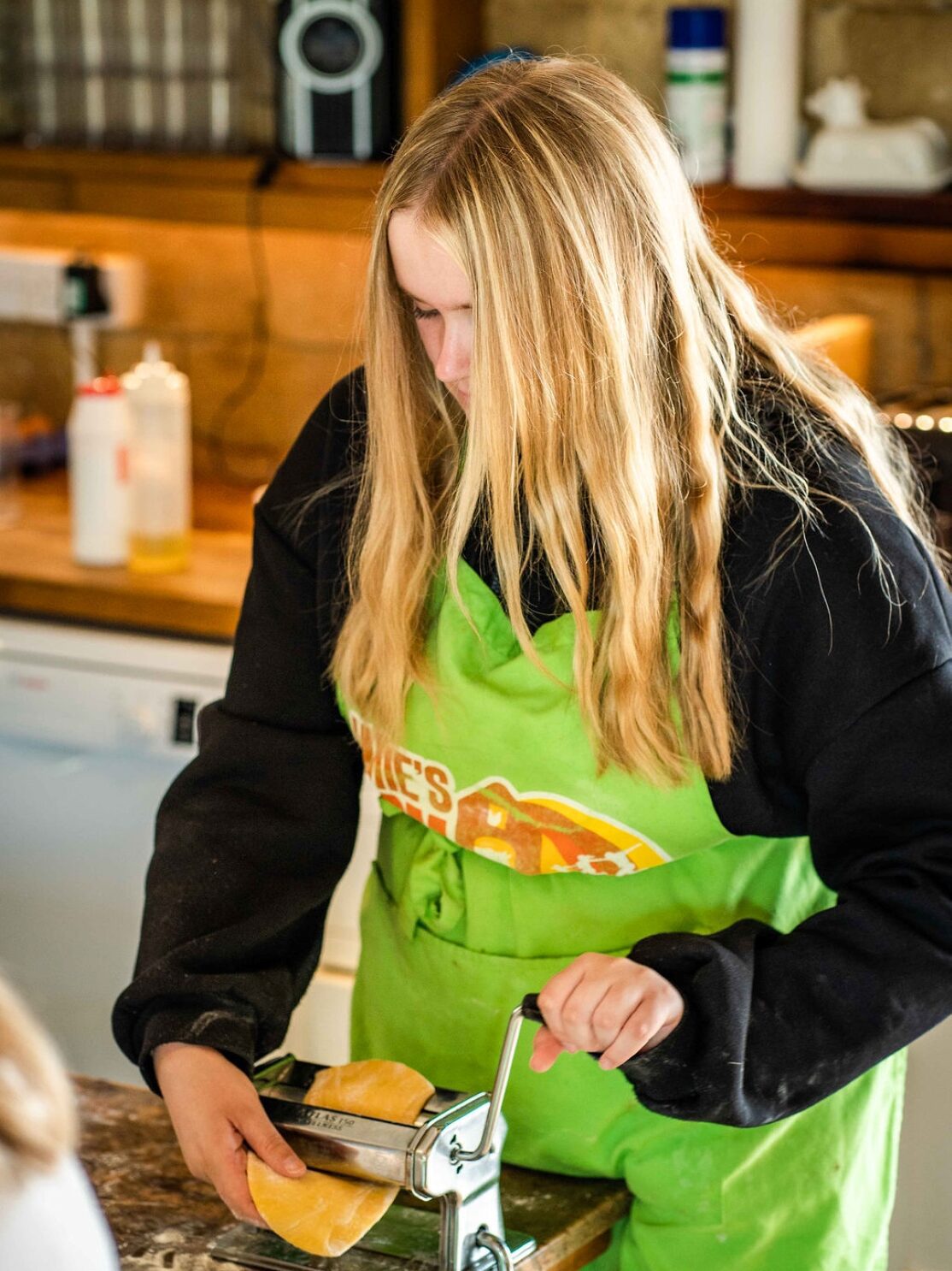 Girl in green apron pressing pasta through a pasta machine