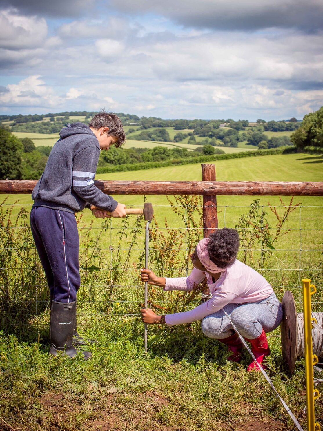 Two young people hammering a pole to mend a fence