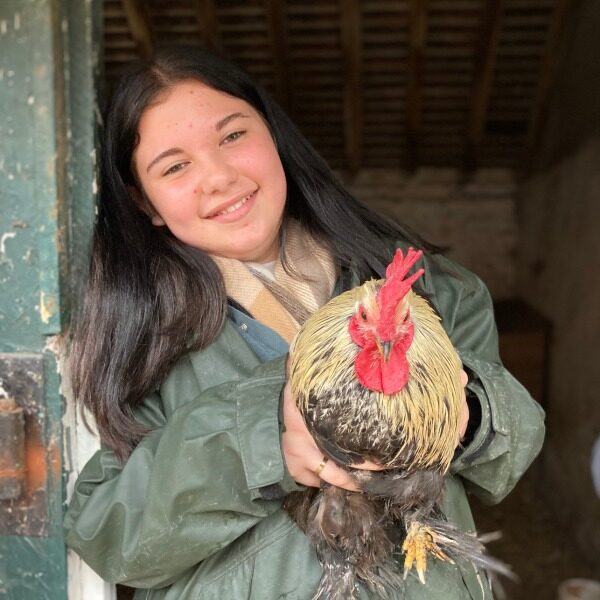 A girl holding a rooster while wearing a green rain-coat