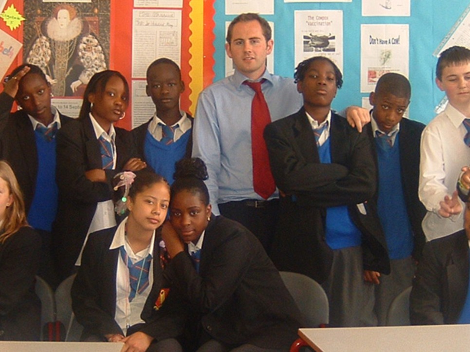 Jamie Feilden of Jamie's Farm stands, wearing a blue shirt and red tie, in the middle of a group of high-school students all dressed in uniform