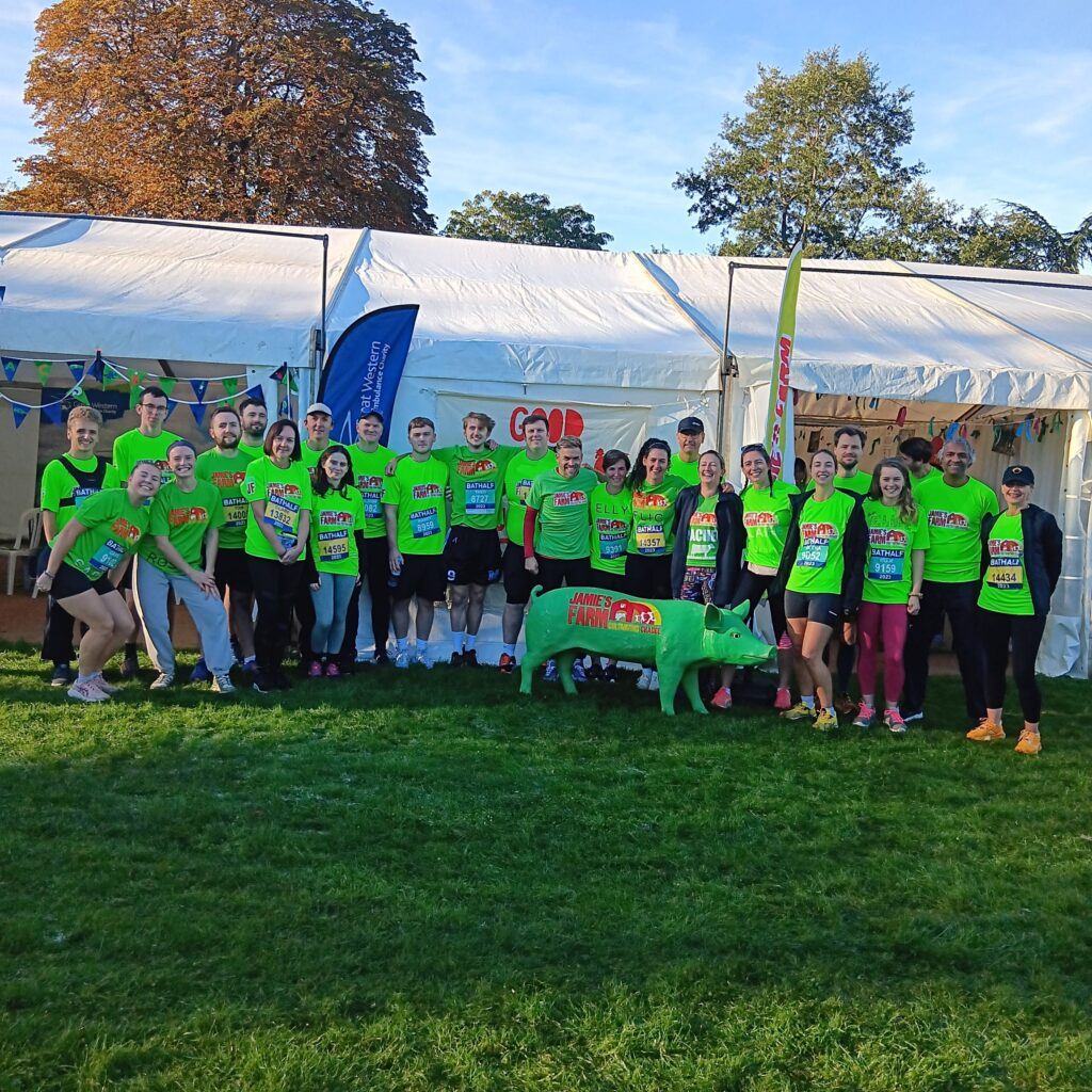 A large group of Bath Half runners in Jamie's Farm green tshirts standing infront of a marquee waving