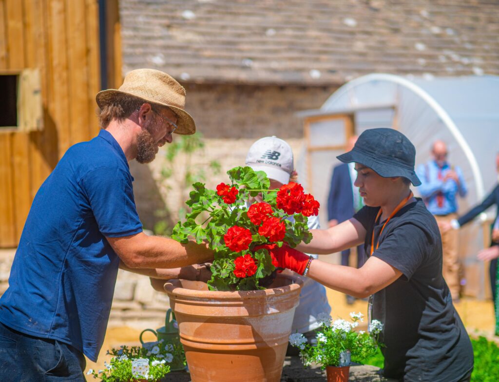 Two people tending to a pot of red flowers.