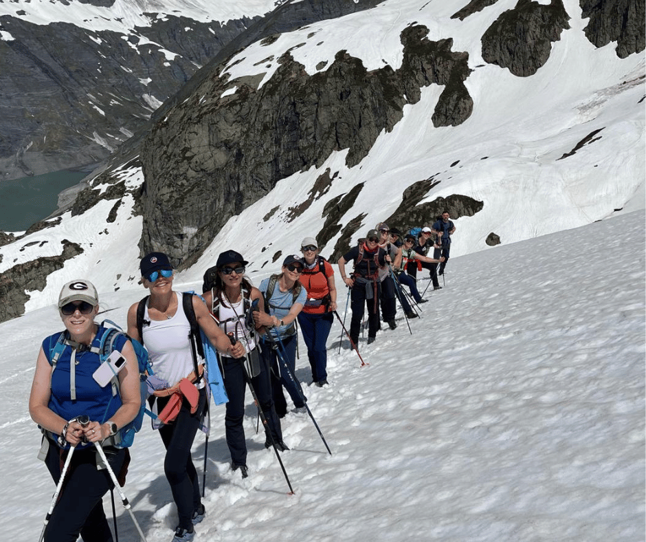 Group of adults with hiking gear walking along a snow covered hill in the Alps.