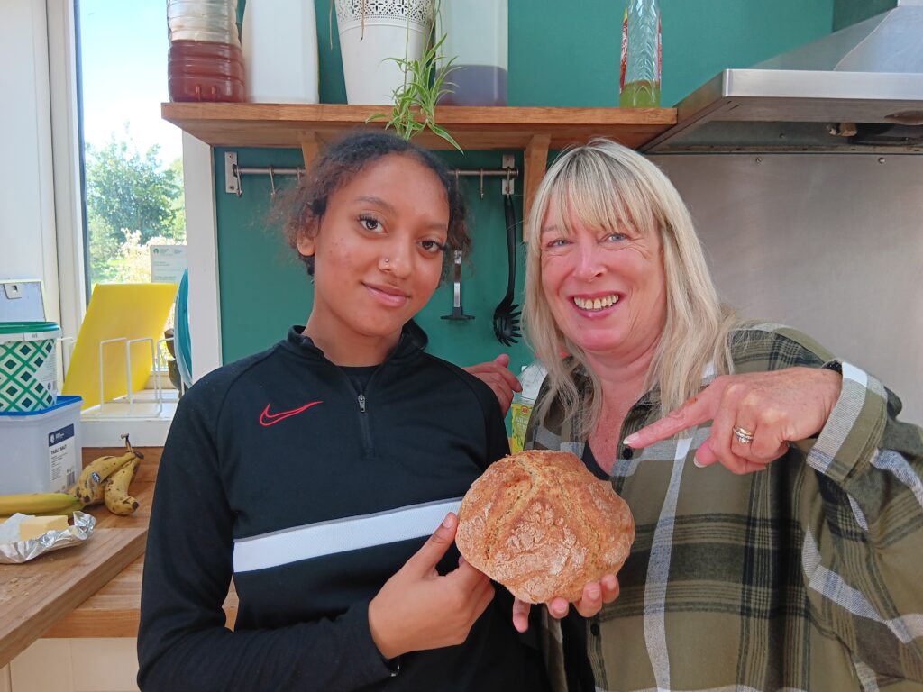 A young person and their staff pointing to a baked loaf of bread they made at Monmouth farm.
