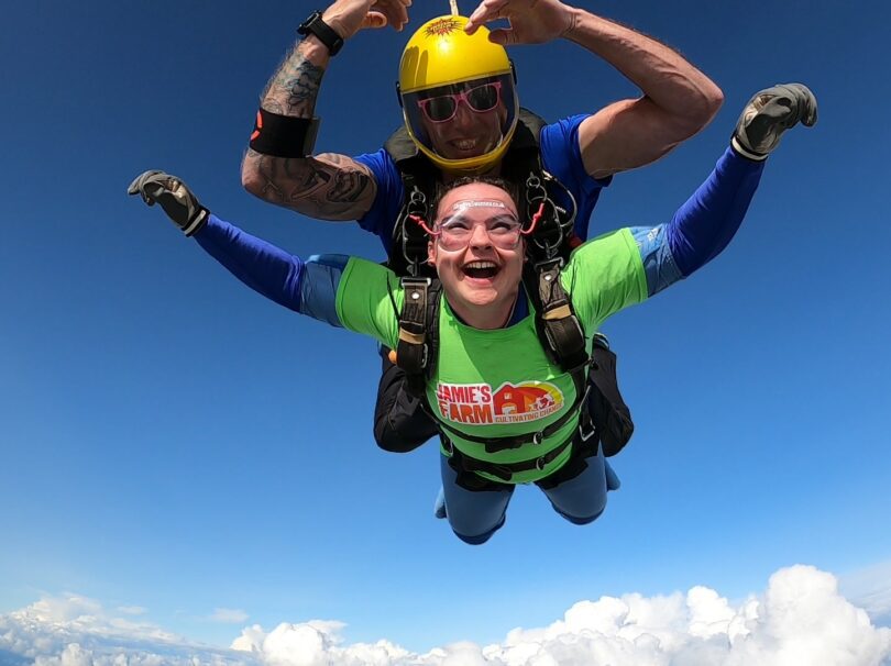 Two people sky diving with blue sky and white clouds behind them