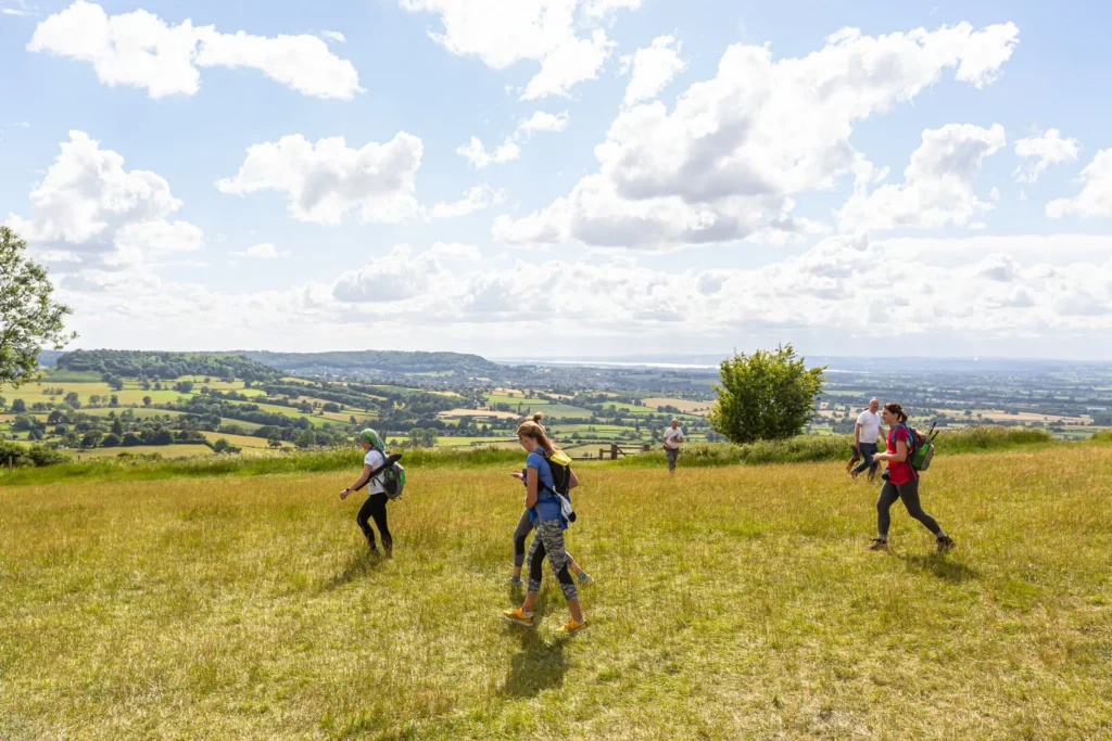 Group of people walking through a grass field on a sunny day with hills in the background.