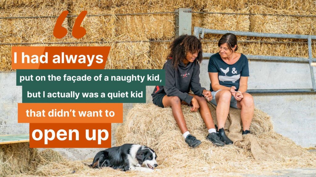 Young person sitting next to an adult on a hay bale with a dog lying down next to them.