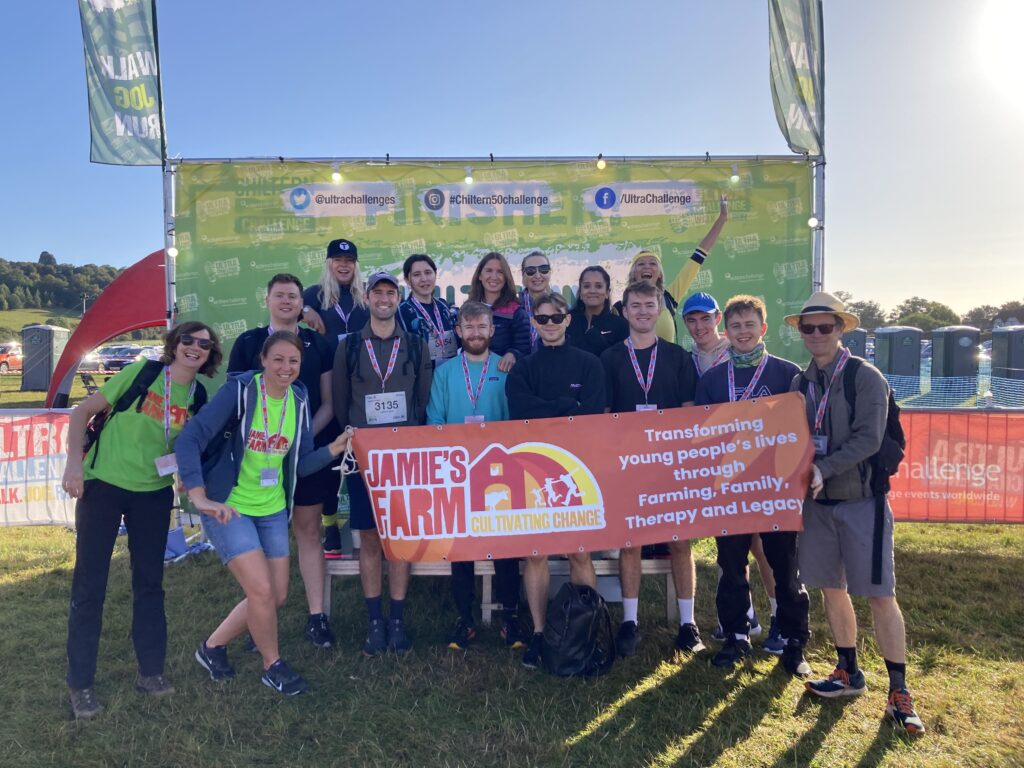 Group of people smiling and wearing Jamie's Farm t-shirts holding a Jamie's Farm banner.