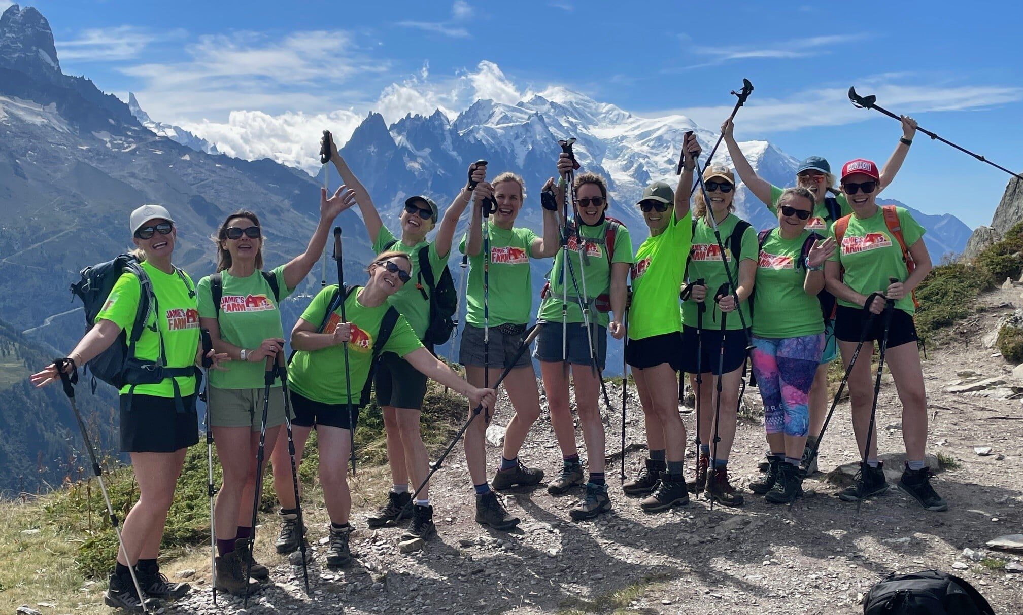 Group of adults in Jamie's Farm tshirts on a mountain in the Alps cheering with their hands up