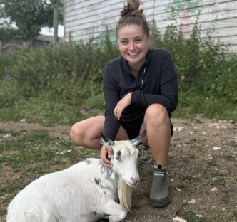 Megan crouching down patting a goat on the farm
