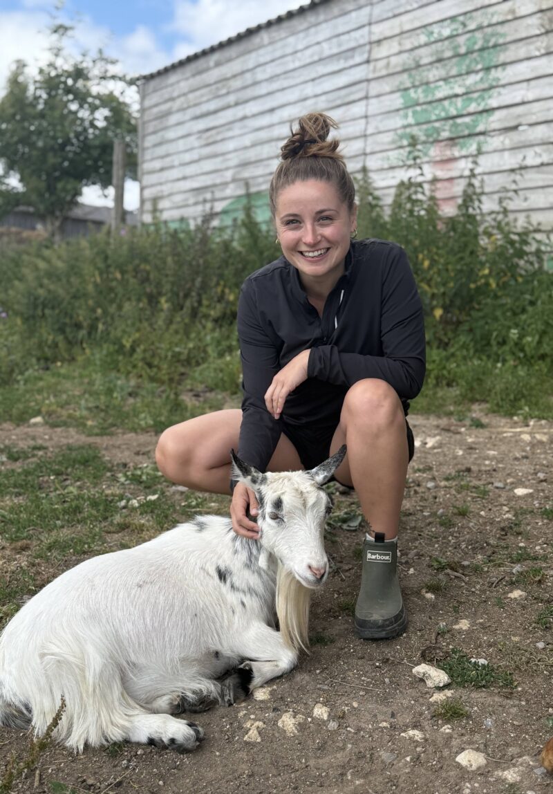 Megan crouching down patting a goat on the farm