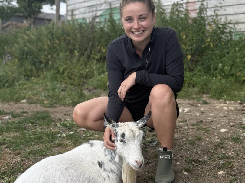 Megan crouching down patting a goat on the farm