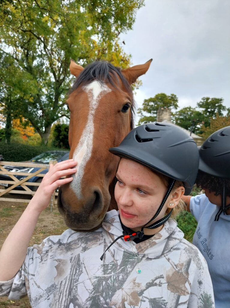 Girl with helmet stroking a horses head.