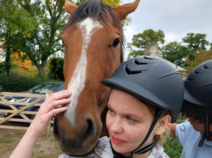 Girl with helmet stroking a horses head.