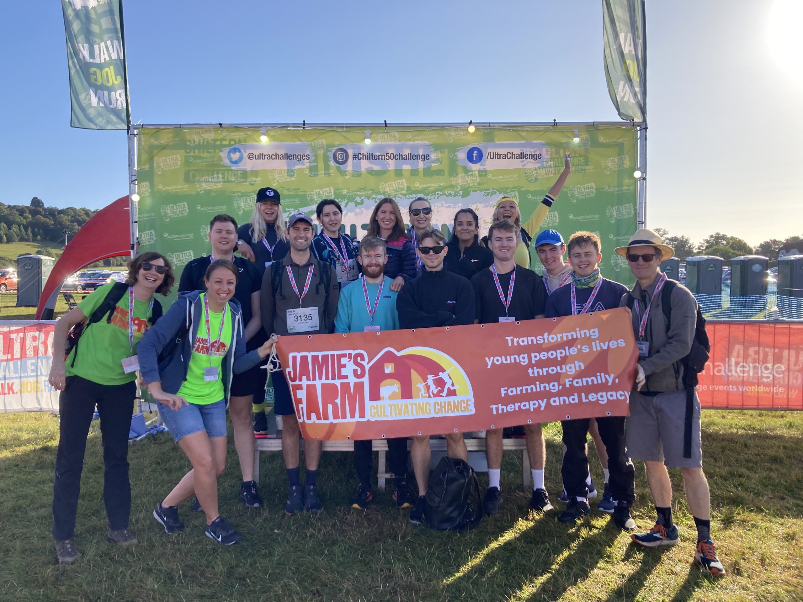A group of 20 or more people on a hill on a sunny day holding a Jamie's Farm banner ahead of the Chiltern Challenge. 