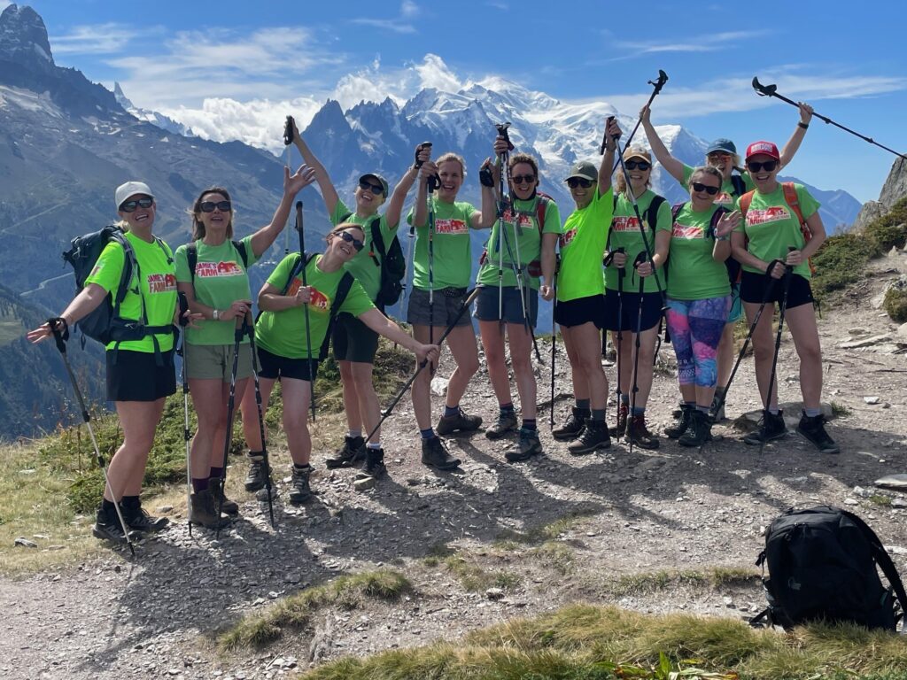 A group of hikers raising their walking sticks, all wearing Jamie's Farm green t-shirts with mountains behind them. 