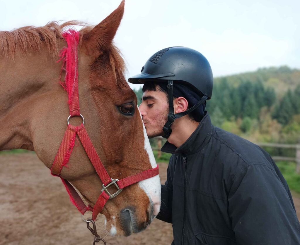 Teenage boy wearing a riding helmet kissing a horse on its forehead in a serene and calm horse work session.