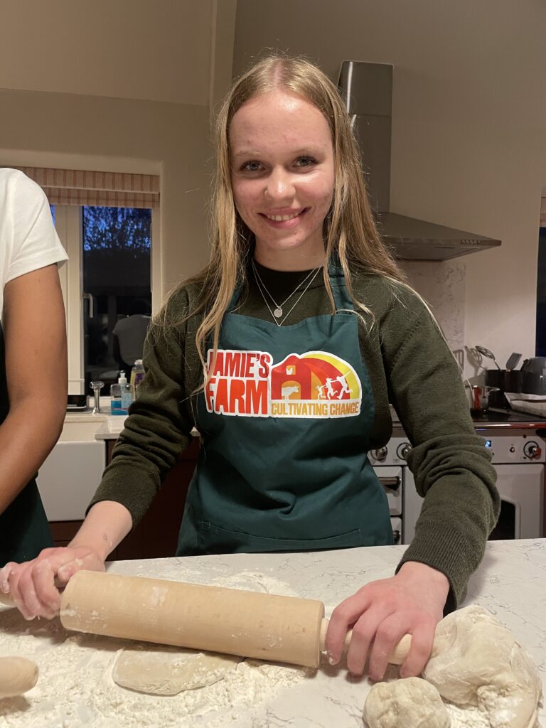 Girl with Jamie's Farm apron on rolling pastry in a kitchen