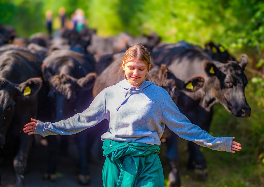 Girl with arms out wearing farm overalls with cows behind her