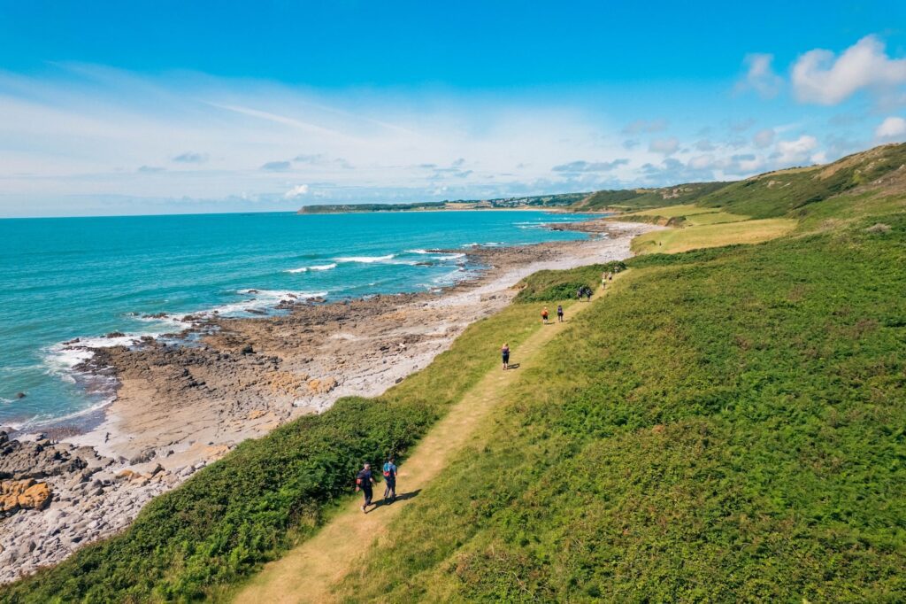 People walking along a coastline with rocks and a blue sea.
