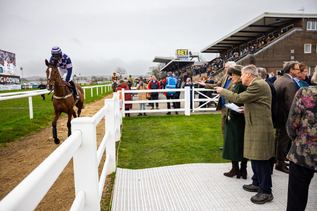 Her Majesty and other guests outside watching a horse run past on the racetrack