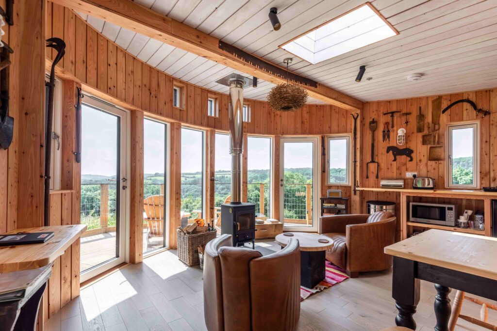 Wooden cabin interior in with leather seats, log burner, table, and far reaching views across Wye Valley
